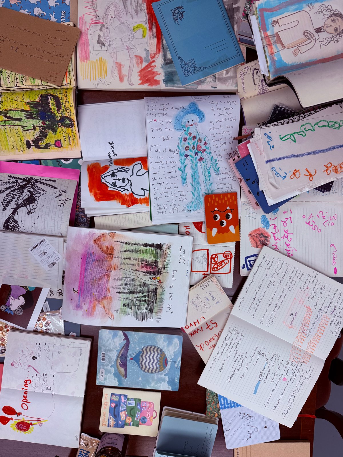 Overhead view of scattered children's artwork and school papers on a wooden floor, including drawings, writings, and colored sketches
